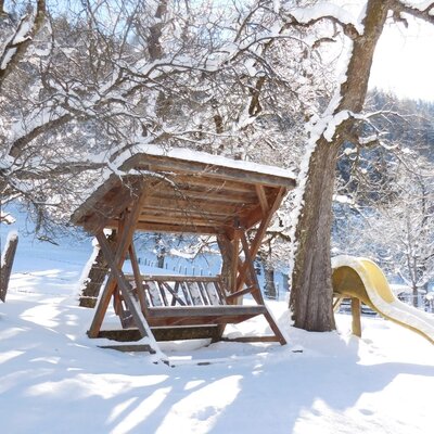 Schneebedeckte Hollywoodschaukel und Rutsche im Außenbereich des Bauernhofs.