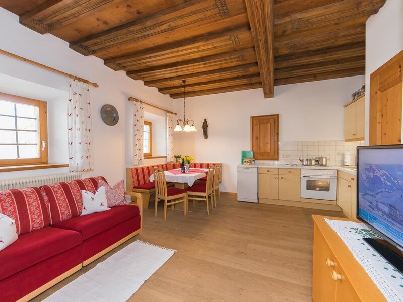 Wohnküche der Ferienwohnung auf dem Bauernhof mit roter Couch, Essbereich, ausgestatteter Küchenzeile und Fernseher.