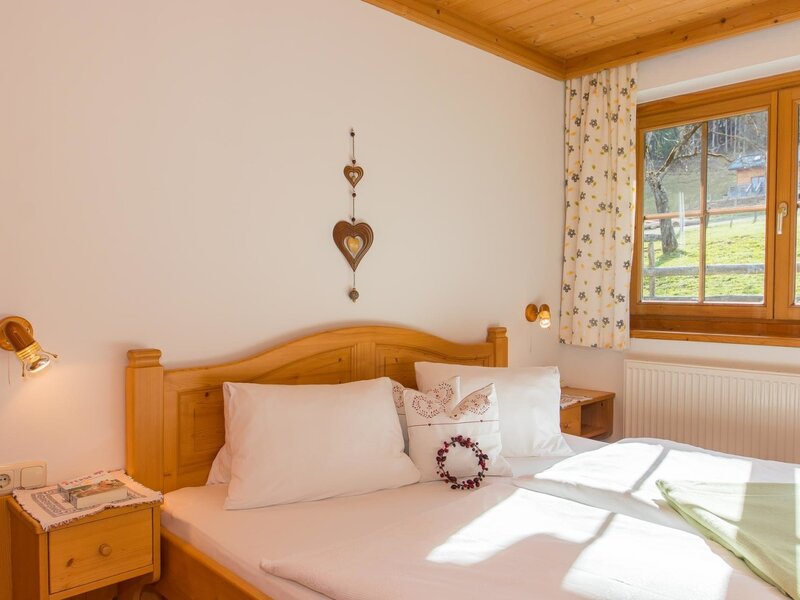 Doppelzimmer der Ferienwohnung auf dem Bauernhof mit Holzdoppelbett, Nachttischen, Leselampen und Fensterblick ins Grüne.