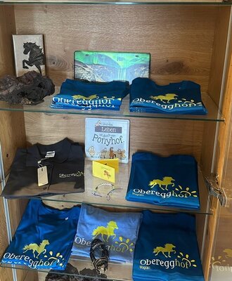 Ein charmant gestaltetes Holzregal auf dem Bauernhof mit gebrandeten T-Shirts und Souvenirs des Hauses.