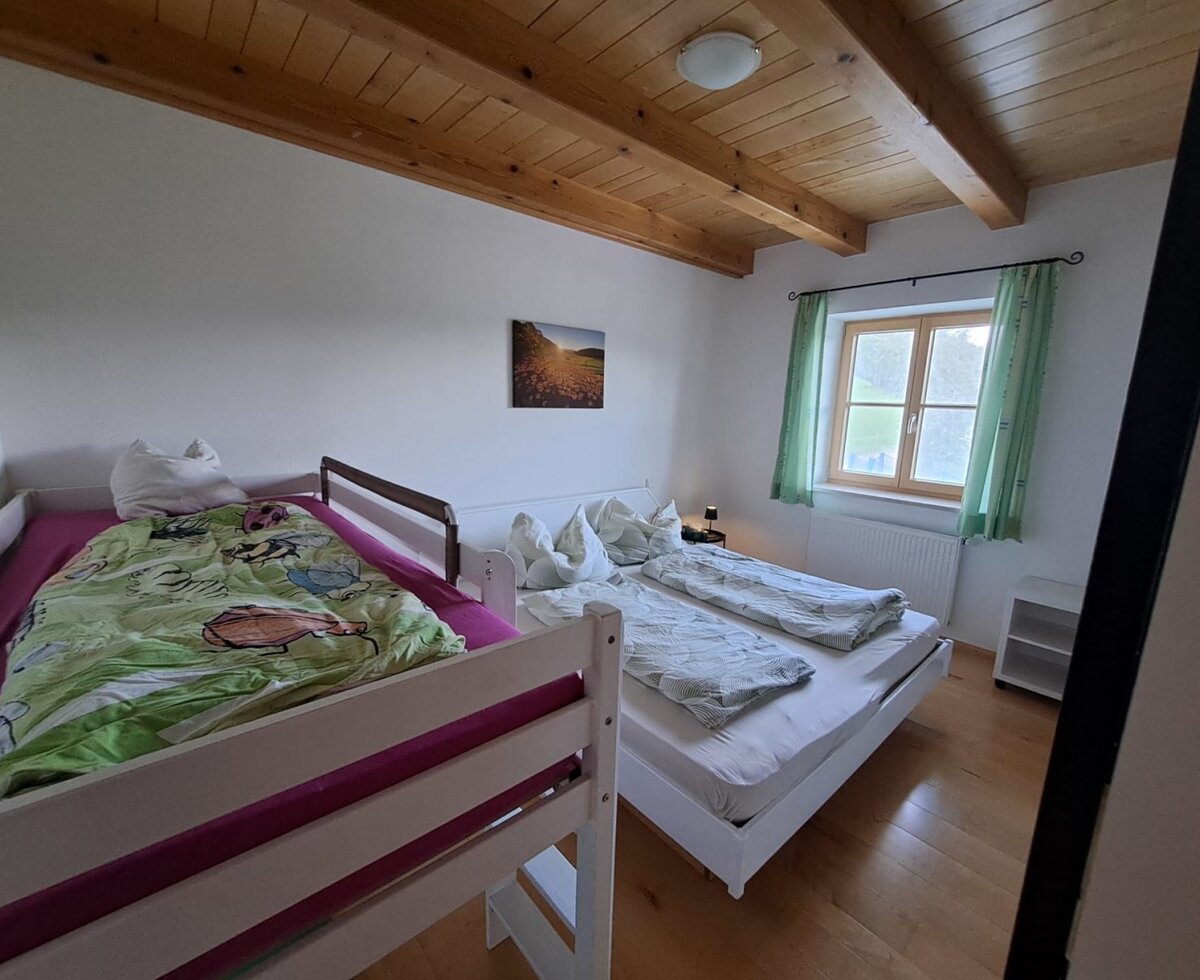 Schlafzimmer in der Ferienwohnung mit Doppelbett, Hochbett, Fenster und Holzbalkendecke.
