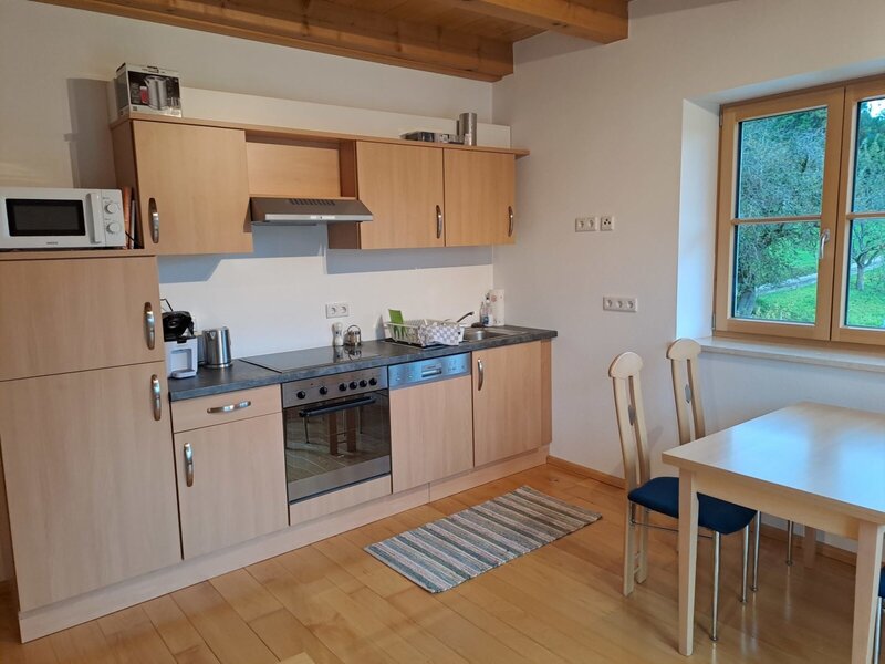 Die voll ausgestattete Küche der Ferienwohnung mit Herd, Backofen, Mikrowelle, Kühlschrank und einem Essbereich am Fenster.