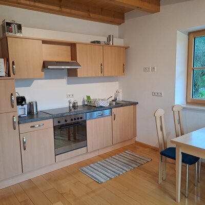 Die voll ausgestattete Küche der Ferienwohnung mit Herd, Backofen, Mikrowelle, Kühlschrank und einem Essbereich am Fenster.