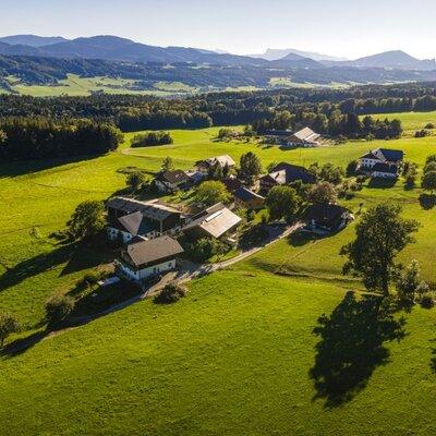 Der einladende Bauernhof aus der Vogelperspektive, eingebettet in saftig grüne Wiesen und eine malerische Hügellandschaft.