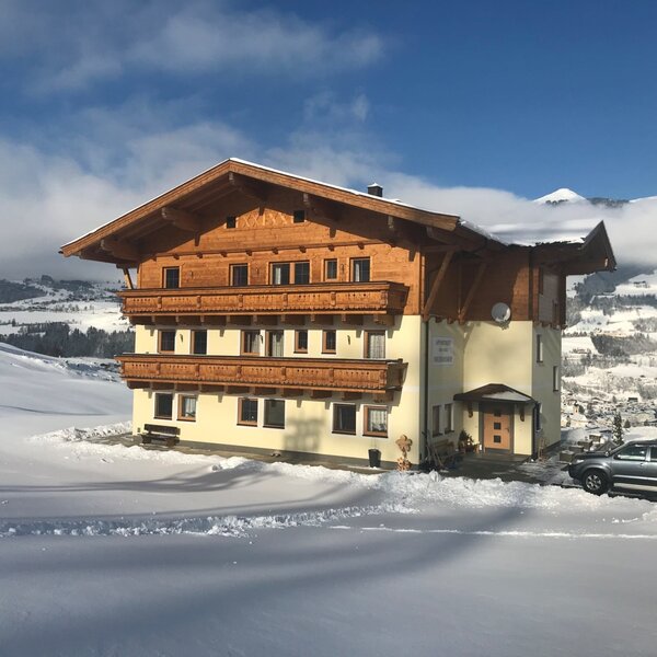 Außenansicht des Bauernhofs mit traditioneller Holzfassade und Balkonen, umgeben von Schnee und Bergen.