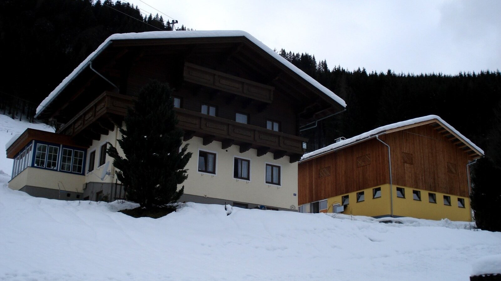 Außenansicht des Bauernhofs im Winter mit Schnee, Balkonen und angrenzendem Wintergarten.