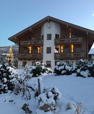 Der Bauernhof in winterlicher Umgebung mit Holzbalkonen und einem geschmückten Weihnachtsbaum.