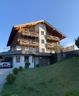 Der Bauernhof mit traditioneller Holzfassade, mehreren Balkonen und einem überdachten Stellplatz.