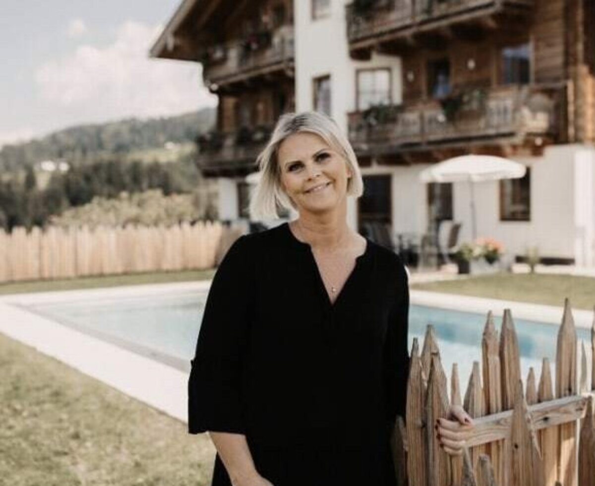 Die Gastgeberin des Bauernhofs vor dem Außenpool und dem Gebäude mit traditioneller Architektur.