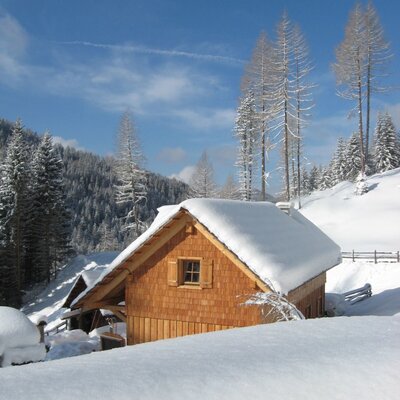 Außenansicht des Hofs mit einem schneebedeckten Holzgebäude in winterlicher Berglandschaft.