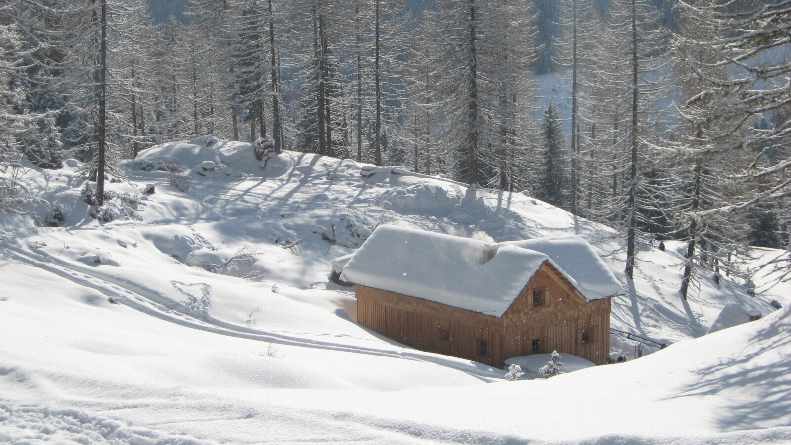 Die verschneite Holzhütte des Hofs in einer Winterlandschaft, mit Rauch aus dem Kamin.