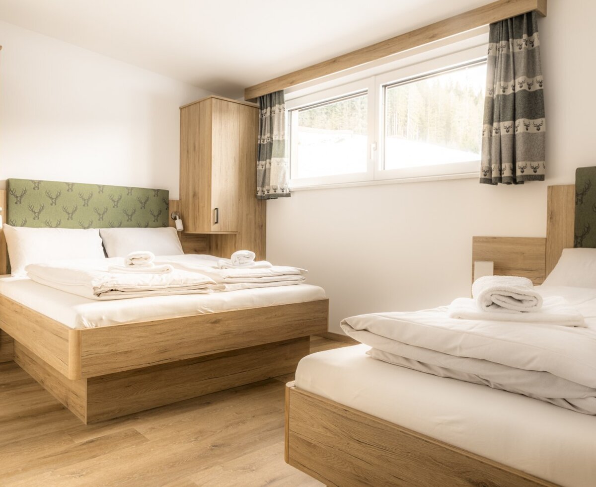 Schlafzimmer mit einem Doppelbett, einem Einzelbett, Holzmöbeln und einem Fenster.