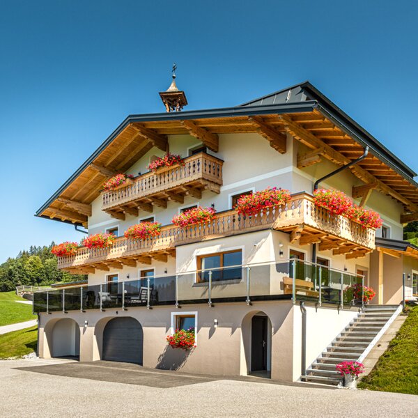 Der einladende Bauernhof mit traditionellen, blumengeschmückten Holzbalkonen inmitten von saftig grünen Bergwiesen.