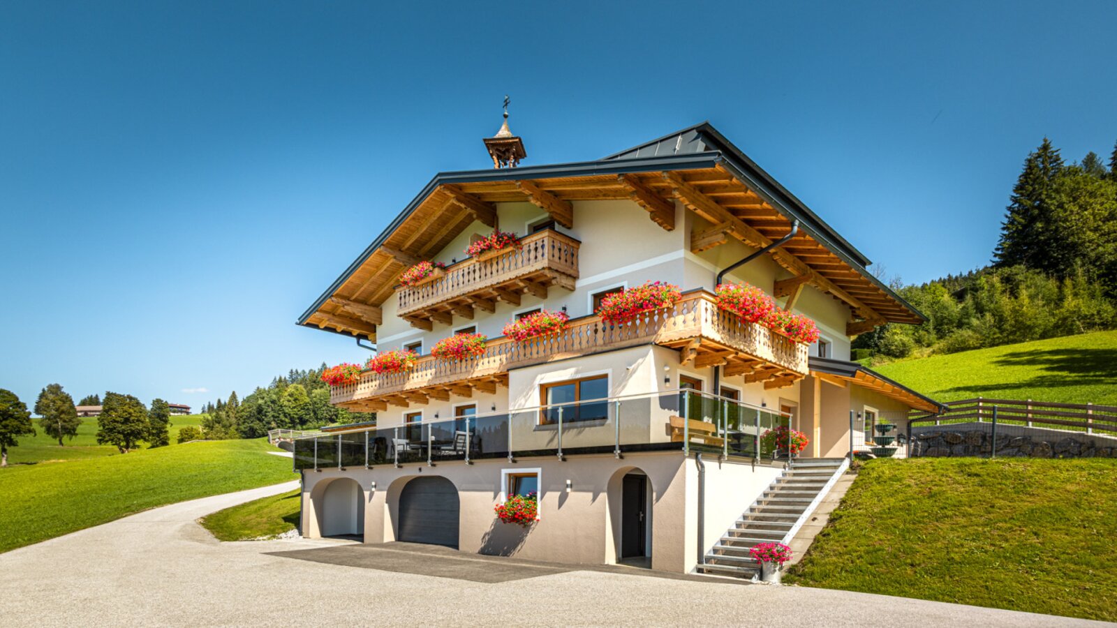 Der einladende Bauernhof mit traditionellen, blumengeschmückten Holzbalkonen inmitten von saftig grünen Bergwiesen.