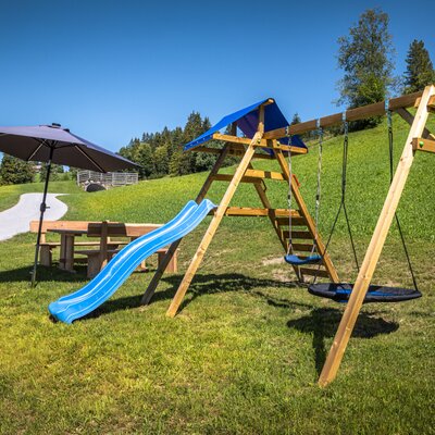 Der einladende Spielplatz des Bauernhofs mit Schaukeln, einer Rutsche und einer gemütlichen Sitzecke im Grünen.