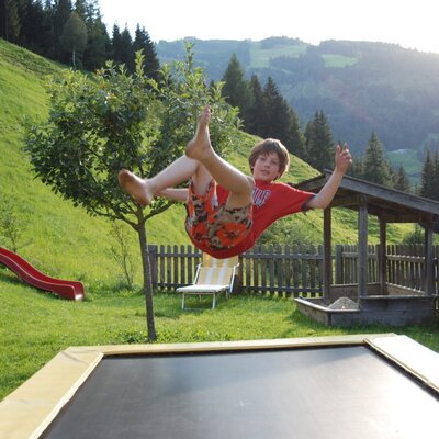 Spielbereich im Freien des Bauernhofs mit Trampolin, Rutsche und Sandkasten.