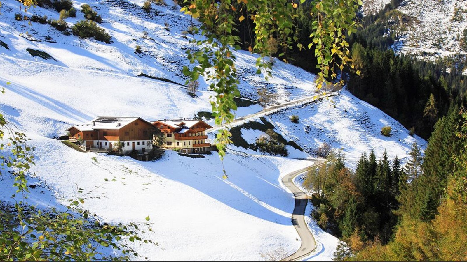 Der Bauernhof umgeben von schneebedeckten Hängen und einer Zufahrtsstraße.