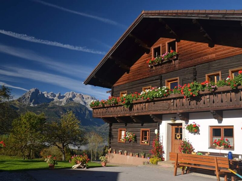Außenansicht des Bauernhofs mit blumengeschmücktem Balkon, Sitzbank und Bergblick.