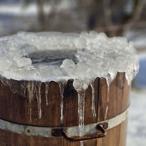 Ein mit Eis und Eiszapfen bedecktes Holzfass auf dem Bauernhof.