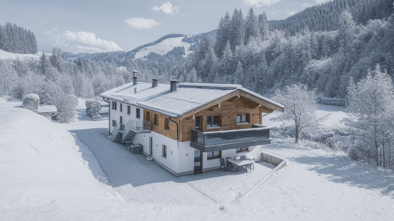 Der Bauernhof im Winter, mit schneebedeckten Bergen und Bäumen im Hintergrund, verfügt über einen Balkon und eine Terrasse mit Sitzgelegenheiten.