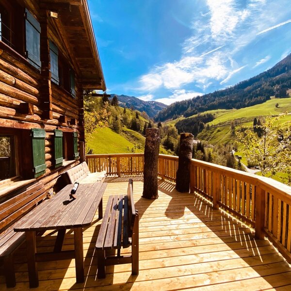 Sonnige Holzterrasse der Alm mit einer gemütlichen Sitzecke und herrlichem Blick auf die umliegende Berglandschaft.