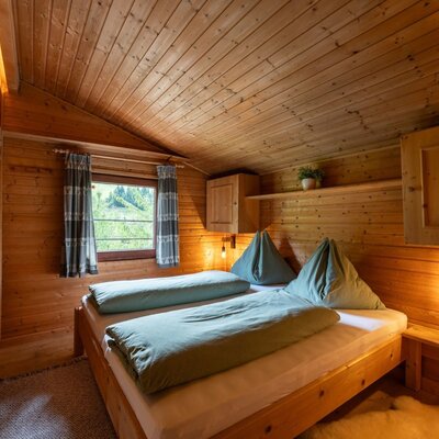 Ein gemütliches Schlafzimmer der Alm mit rustikaler Holzvertäfelung, einladenden Betten und warmer Beleuchtung.
