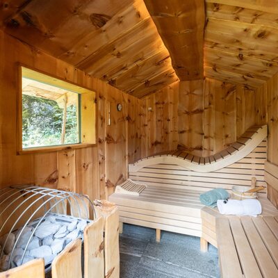 Die einladende Sauna der Alm mit gemütlichen Holzbänken, einem großen Fenster und warmem Licht.