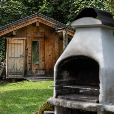 Der einladende Außenbereich der Alm mit einem gemauerten Grill und einer urigen Holzhütte im Hintergrund.