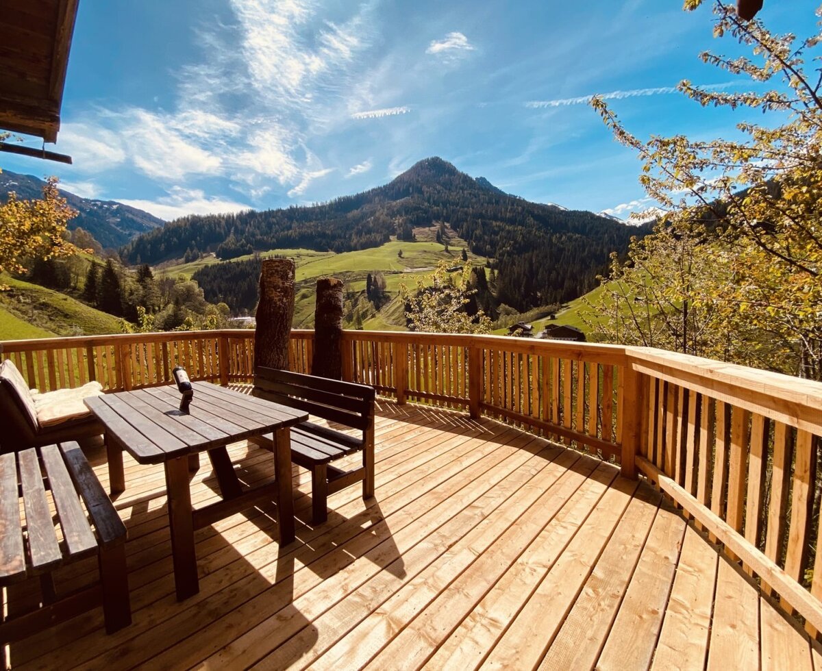 Die sonnige Holzterrasse der Alm mit gemütlicher Sitzgruppe und herrlichem Blick auf die umliegenden Berge.