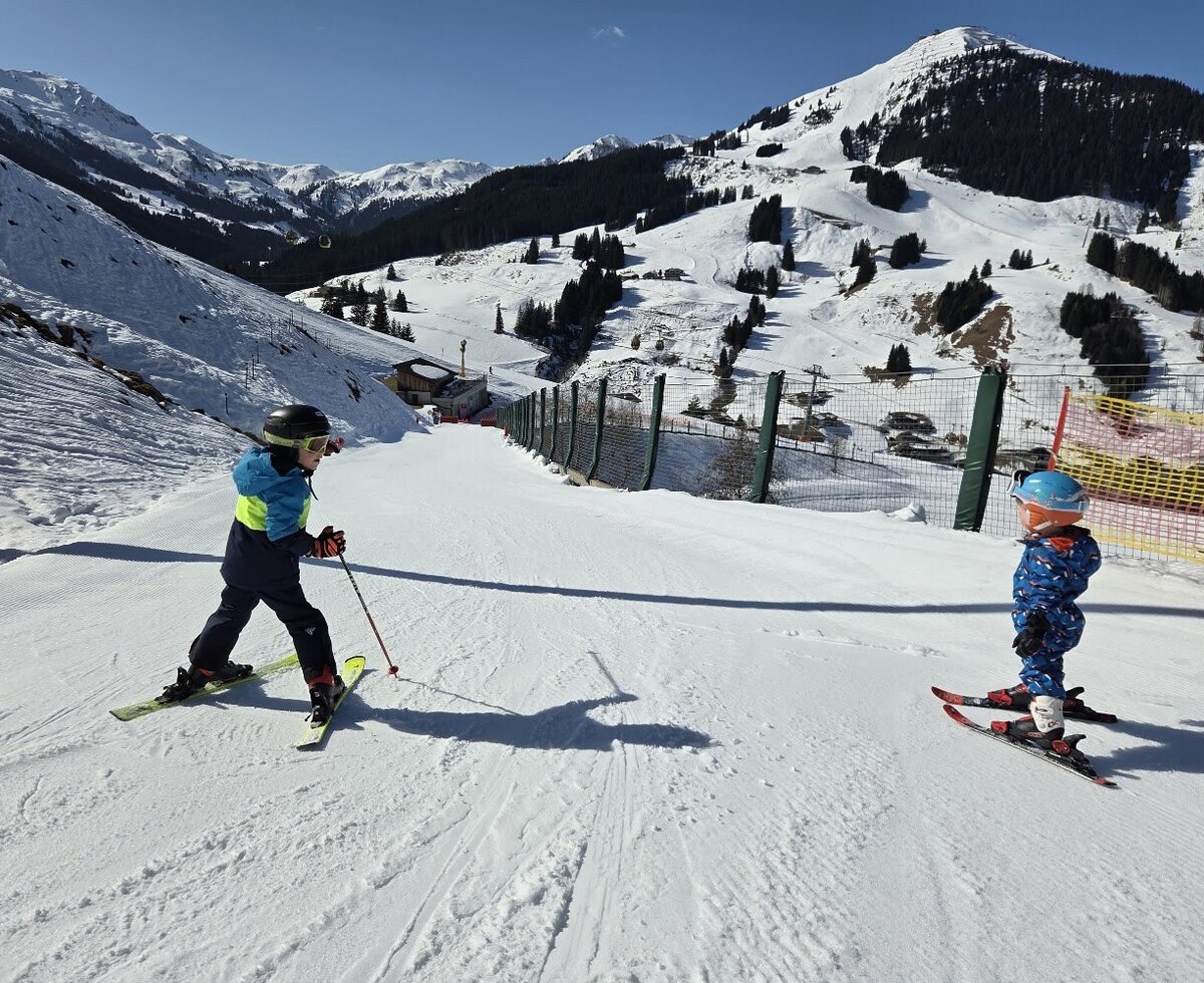 Die sonnige Skipiste in der Nähe des Bauernhofs mit Blick auf die verschneite Bergkulisse lädt Kinder zum Skifahren ein.