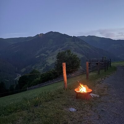Eine gemütliche Feuerschale auf dem Gelände des Bauernhofs mit Blick auf die umliegende Berglandschaft in der Dämmerung.