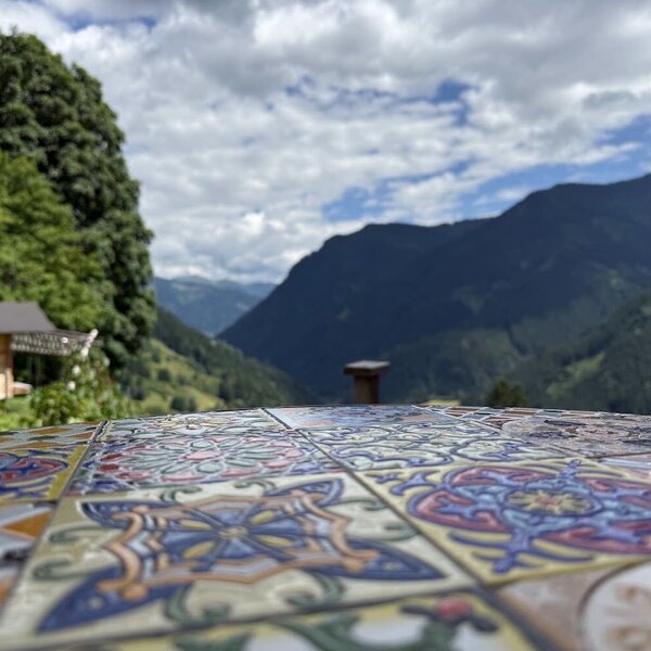 Der einladende Blick vom Bauernhof über einen kunstvoll gefliesten Tisch auf die umliegende Berglandschaft.