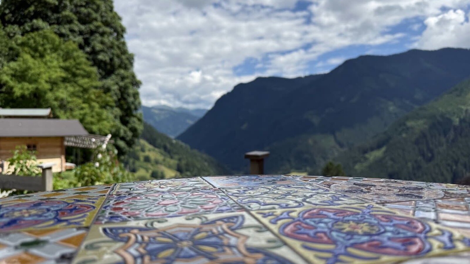 Der einladende Blick vom Bauernhof über einen kunstvoll gefliesten Tisch auf die umliegende Berglandschaft.