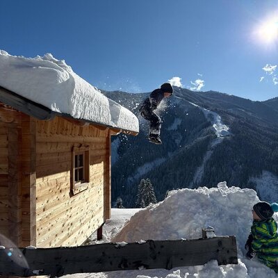 Spielerischer Winterspaß auf dem Bauernhof vor einer malerischen, schneebedeckten Bergkulisse.