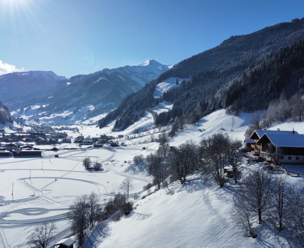 Blick auf den Bauernhof, das verschneite Tal und die umliegenden Berge.