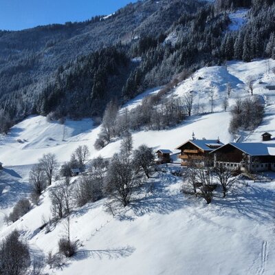 Der Bauernhof in einer verschneiten Berglandschaft mit traditionellen Gebäuden und Blick auf die Berge und das Tal.