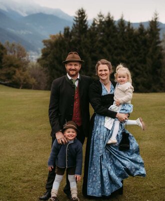 Die Gastgeberfamilie des Bauernhofs in traditioneller Kleidung mit Kindern vor Bergkulisse.