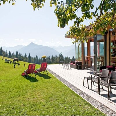 Die Terrasse des Hofes mit Sitzbereichen und Liegestühlen bietet einen direkten Blick auf die Berge und die angrenzende Wiese mit Bauernhoftieren.