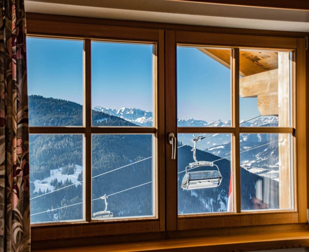 Fenster mit Blick auf schneebedeckte Berge, Wälder und Skilifte vom Bed and Breakfast.