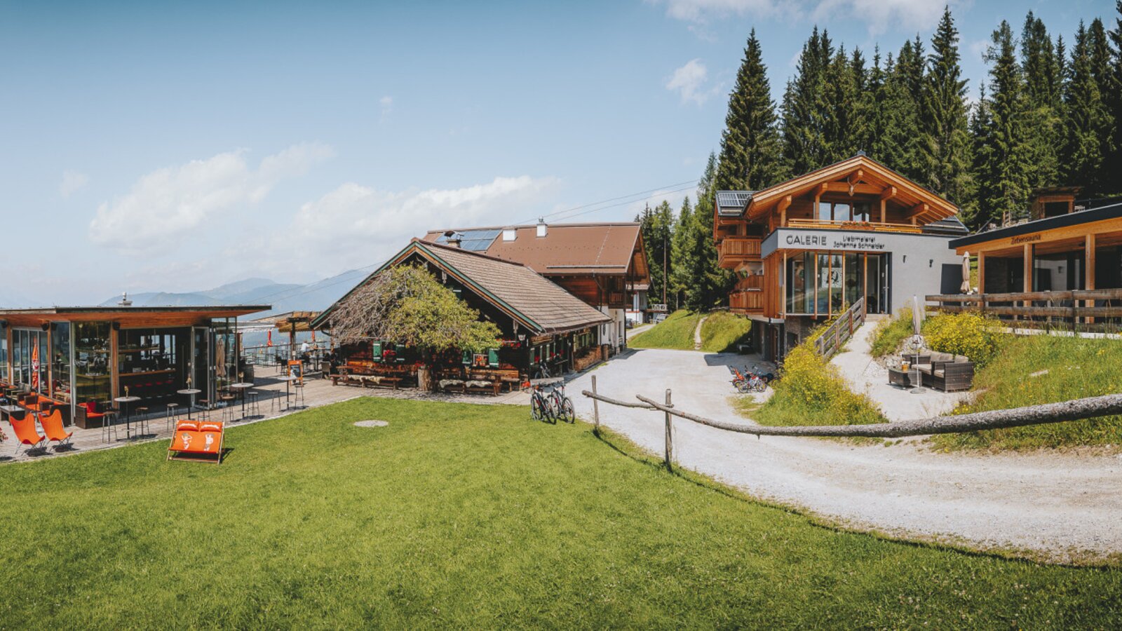 Der Hof mit verschiedenen Gebäuden, einem Terrassenbereich mit Liegestühlen und Gastronomie sowie Bergblick.