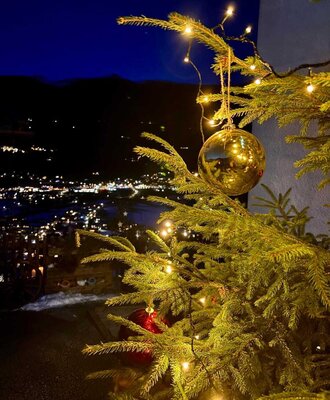 Stimmungsvoll dekorierter Baum mit Blick auf das beleuchtete Tal und die Berge vom Bauernhof.