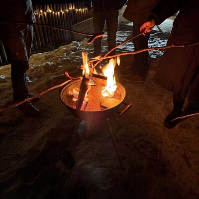 Abendliche Feuerstelle auf dem Bauernhof, wo Gäste im Schnee Würstchen braten können.