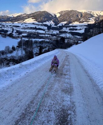 Rodelausflug auf einer verschneiten Straße mit Blick auf die winterliche Berglandschaft vom Bauernhof aus.