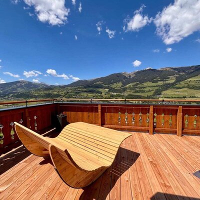 Große Liegeterrasse des Bauernhofs mit gemütlichen Holzliegen und Blick auf die Berge und das Salzachtal.