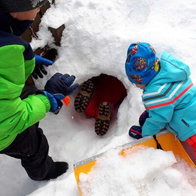 Kinder beim Spielen im Schnee und Erkunden einer Schneehöhle auf dem Bauernhof.