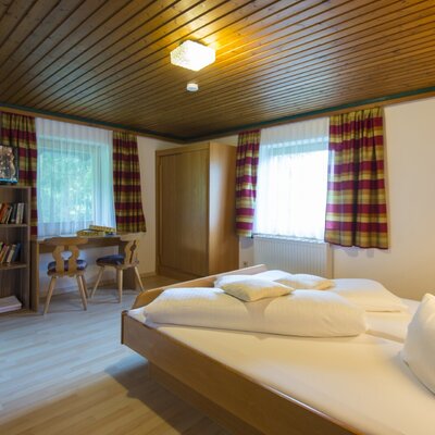 Doppelzimmer im Bauernhof mit Doppelbett, Holzkleiderschrank, Schreibtisch, Bücherregal und Fernseher.