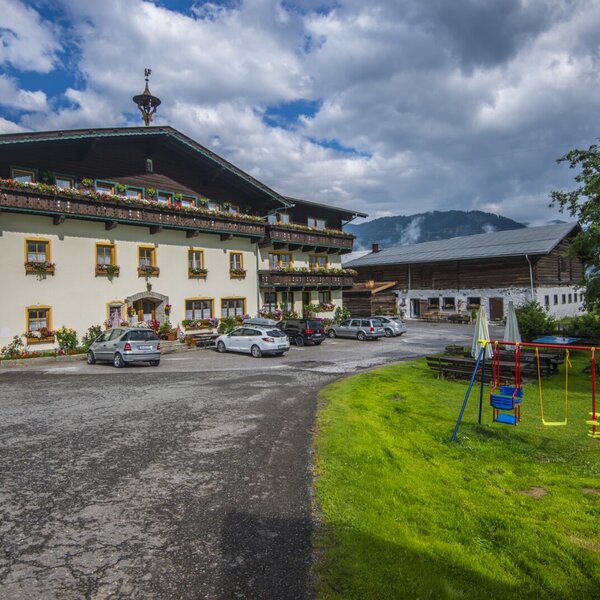 Der Bauernhof mit Parkplatz und einem Spielbereich für Kinder, ausgestattet mit Schaukeln und Liegestühlen.