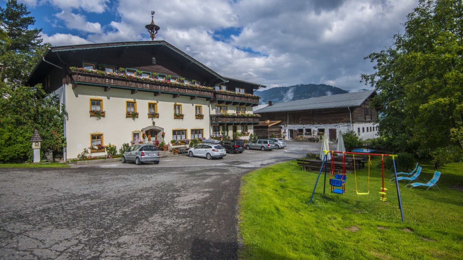 Der Bauernhof mit Parkplatz und einem Spielbereich für Kinder, ausgestattet mit Schaukeln und Liegestühlen.