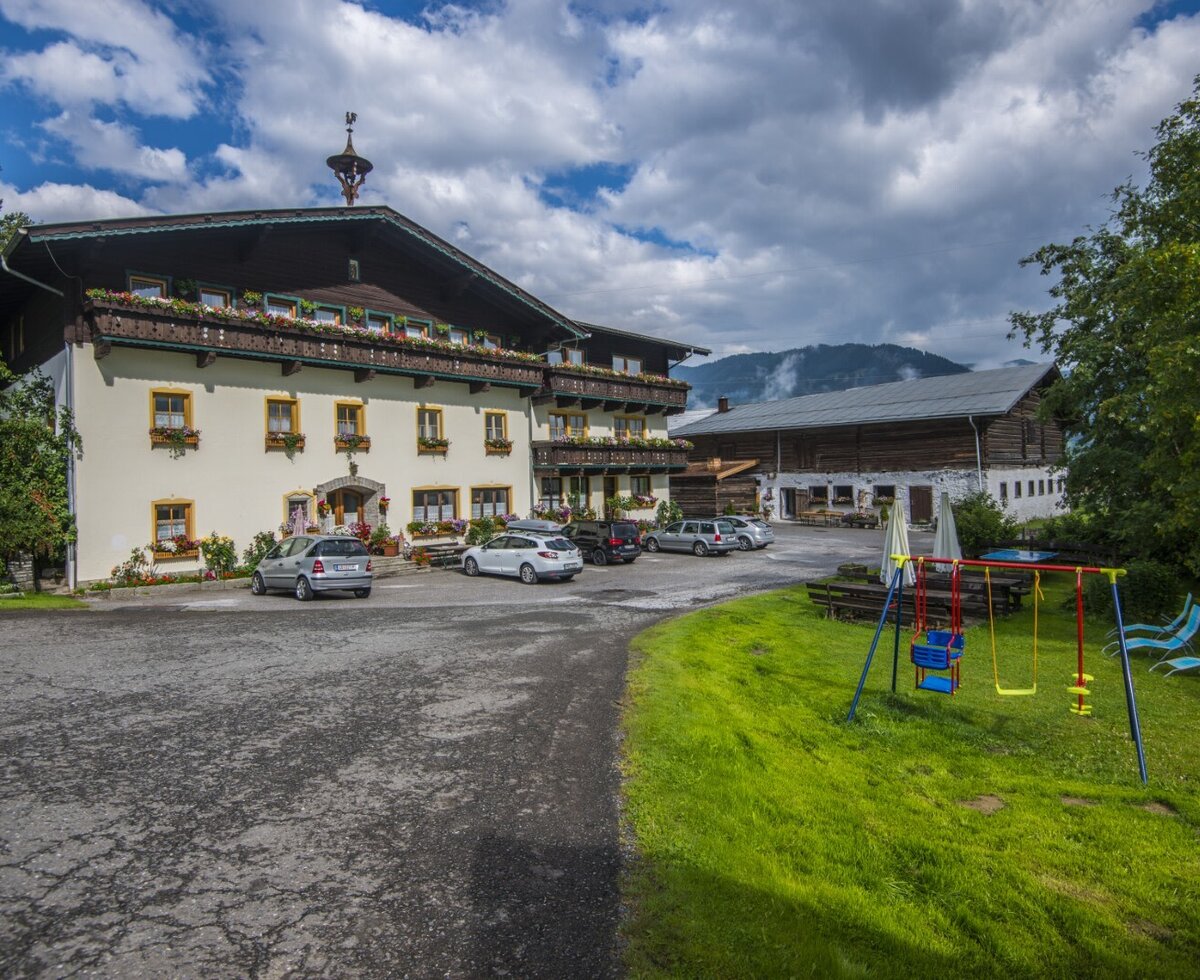 Der Bauernhof mit Parkplatz und einem Spielbereich für Kinder, ausgestattet mit Schaukeln und Liegestühlen.