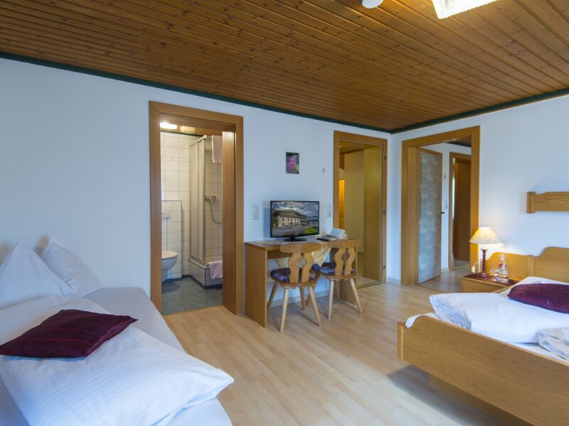 Schlafzimmer im Bauernhof mit Doppelbett, Einzelbett, Schreibtisch, TV und Zugang zu einem Badezimmer mit Dusche und WC.